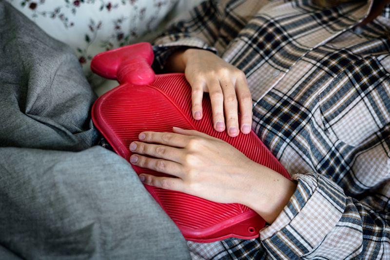 Frau wärmt sich den Bauch mit Wärmflasche im Winter.