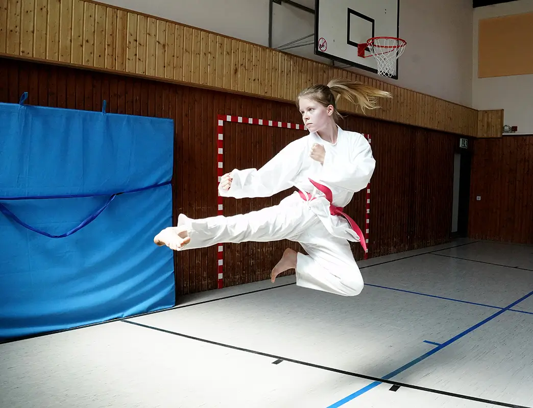 gesprungener Taekwondo Sidekick ausgeführt von einer Dame mit Rotgurt bei ihrer Prüfung zum 1. Dan