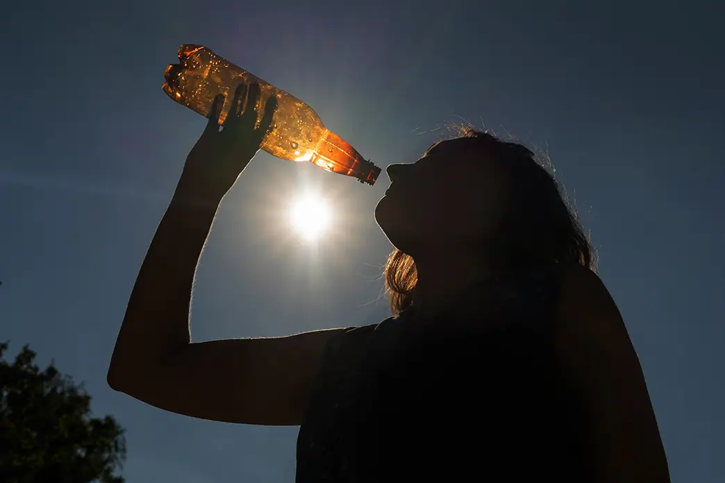 Unter der grellen Sonne trinkt eine Frau Wasser aus einer Flasche